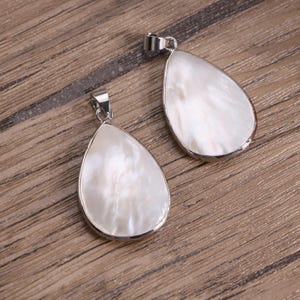 May include: Two teardrop-shaped pendants featuring iridescent white mother-of-pearl inlays set within polished silver-toned metal frames. Each pendant includes a small metal bail at the top for attachment to a necklace chain or cord.