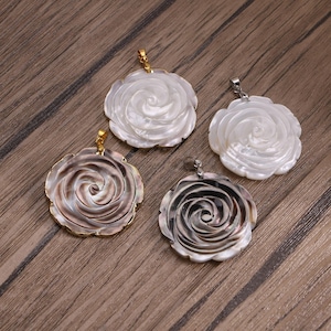 May include: Four circular pendants carved from iridescent shell into the shape of blooming roses. Two pendants are white with a pearlescent sheen, and two are dark grey with metallic undertones. Each pendant features a small metal bail at the top.