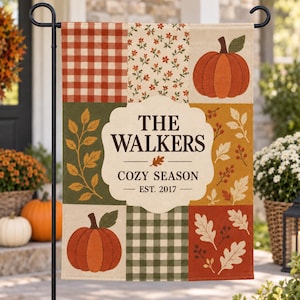 May include: A rectangular garden flag featuring a patchwork design of orange gingham, floral patterns, and autumn leaves. The center displays a cream-colored scalloped label with the text THE WALKERS, COZY SEASON, and EST. 2017, flanked by orange pumpkins.