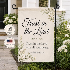 May include: A rectangular garden flag with a cream-colored background featuring watercolor-style green leaves and white flowers. The text reads Trust in the Lord. Trust in the Lord with all your heart. —Proverbs 3:5 in black script and serif fonts.