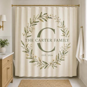 May include: A cream-colored shower curtain featuring a large green letter C centered within a circular botanical wreath of green leaves and small white flowers. The text THE CARTER FAMILY is printed above the letter, with EST. 2026 below it.