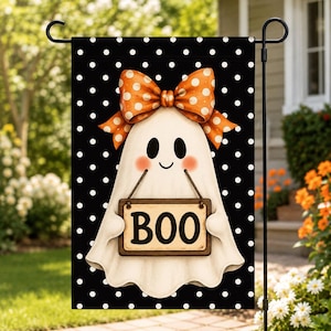 May include: A rectangular garden flag featuring a black background with white polka dots. A white ghost character with pink cheeks and an orange polka-dot bow sits in the center, holding a tan wooden sign with the black text BOO printed on it.