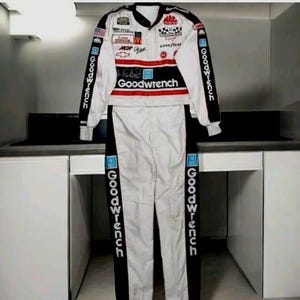 Puede incluir: Un mono de carreras blanco con detalles en negro y rojo, con el texto Goodwrench impreso verticalmente en las mangas y las piernas. El pecho muestra varios logotipos de patrocinadores, incluidos Mac Tools, Goodyear y Chevrolet, junto a una firma.