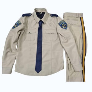 May include: A tan uniform set, comprising a long-sleeved shirt with shoulder epaulettes and a dark blue tie, and matching trousers with a yellow and blue stripe down the side. The shirt has two chest pockets and patches.