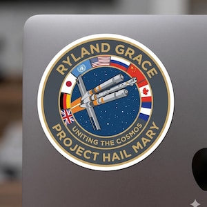 Può includere: Un adesivo circolare con le scritte "RYLAND GRACE" e "PROJECT HAIL MARY". Il design include un'astronave, bandiere di varie nazioni e la frase "Uniting the Cosmos" su uno sfondo spaziale.