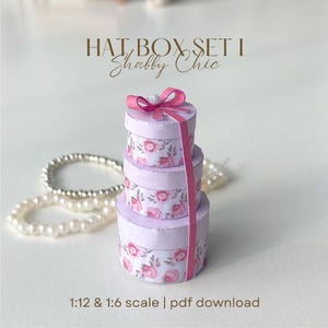 Puede incluir: Tres cajas de sombreros apiladas, de color lavanda, con estampado floral y lazo rosa. Las cajas están atadas con una cinta rosa y rematadas con una perla. El texto dice "HAT BOX SET I Shabby Chic" y "1:12 & 1:6 scale | pdf download".