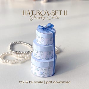 May include: A stack of three round, light blue hat boxes with floral patterns and a matching blue ribbon. The boxes are labeled "HAT BOX SET II Shabby Chic" and are available as a PDF download in 1:12 and 1:6 scale.