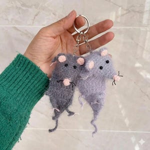 May include: Two handmade mouse keychains. One mouse is gray, the other is lavender. Both have pink ears and noses, black eyes, and black whiskers. The keychains are attached to a silver keyring.