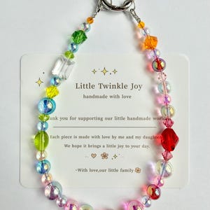 May include: A colorful beaded keychain with a silver clasp. The beads are a mix of clear, iridescent, and brightly colored shapes. A card behind the keychain reads "Little Twinkle Joy handmade with love."