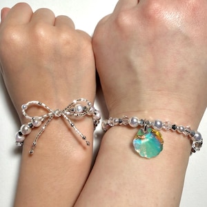 May include: Two beaded bracelets. One bracelet features a bow design with pearls and silver beads. The other bracelet has pearls, silver beads, and a colorful iridescent charm.
