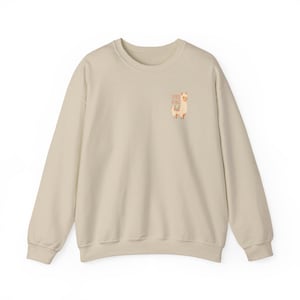 Peut inclure: Un sweat-shirt beige à col rond. Il présente un petit motif de lama avec le texte "Alpaca My Bags". Le sweat-shirt est fabriqué dans une matière douce, idéale pour un usage quotidien.