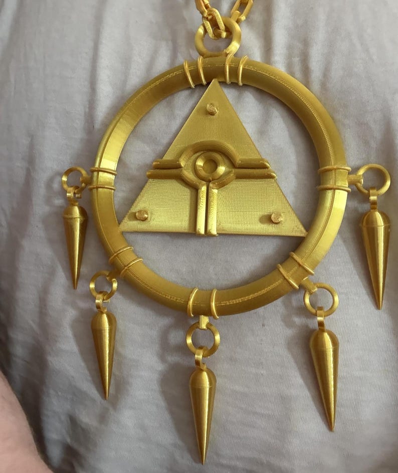 May include: Gold-colored pendant necklace featuring a central triangle with an eye design, surrounded by a circular frame. The pendant has several cone-shaped dangles. The necklace is made of a gold-colored material.