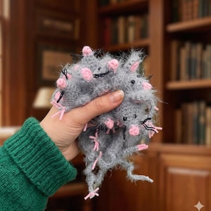 Puede incluir: Un grupo de ratones grises y difusos hechos a mano, con orejas y narices rosas y bigotes negros. Los ratones se sostienen en una mano, con una manga de suéter verde en el fondo. Un artículo artesanal único y caprichoso.