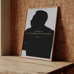 Könnte beinhalten: Gerahmter Kunstdruck mit einer schwarzen Silhouette von Pelé vor hellgrauem Hintergrund. Der goldfarbene Text lautet "A penalty is a cowardly way to score" und "Pelé". Das Kunstwerk wird auf einer Holzoberfläche präsentiert.