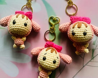 May include: Three handmade crochet keychains featuring a cartoon character with a light yellow head, brown hair, and pink bow. The keychains have pink arms and legs, and gold-colored heart-shaped clasps.