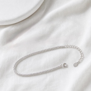 Pode incluir: Uma pulseira de corrente prateada com um design de elos texturizados estilo pipoca. A pulseira inclui um fecho de mola circular e uma corrente extensora ajustável que termina numa pequena etiqueta metálica com a marcação S925 gravada.