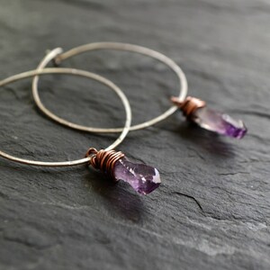 May include: A pair of silver hoop earrings with amethyst crystal accents wrapped in copper wire.