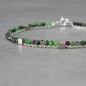 May include: A delicate silver chain bracelet with green and pink gemstone beads and silver square accents.