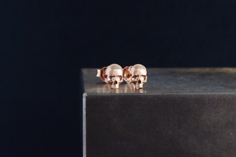 May include: A pair of rose gold skull stud earrings. The earrings are small and delicate, and they are perfect for adding a touch of edgy style to any outfit.