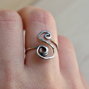 May include: A silver ring with a twisted design in the shape of the letter "S".