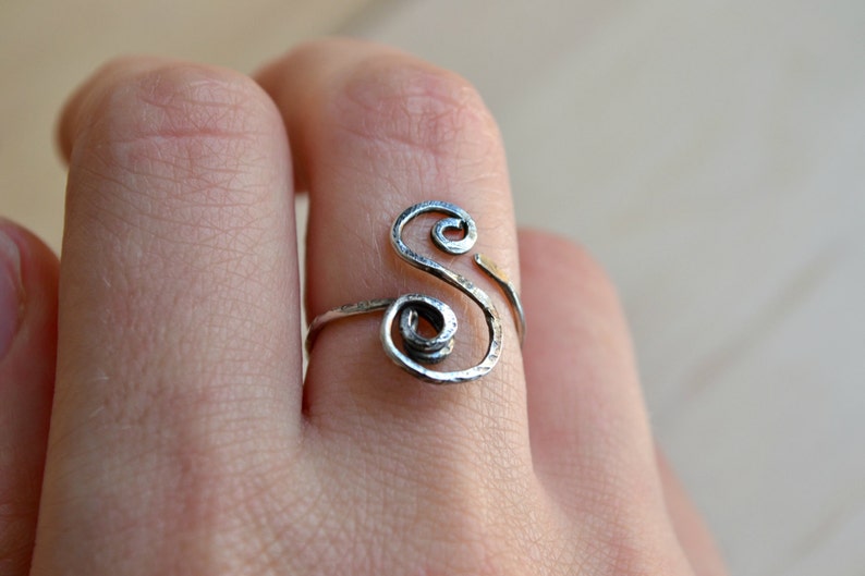 May include: A silver ring with a twisted design in the shape of the letter "S".