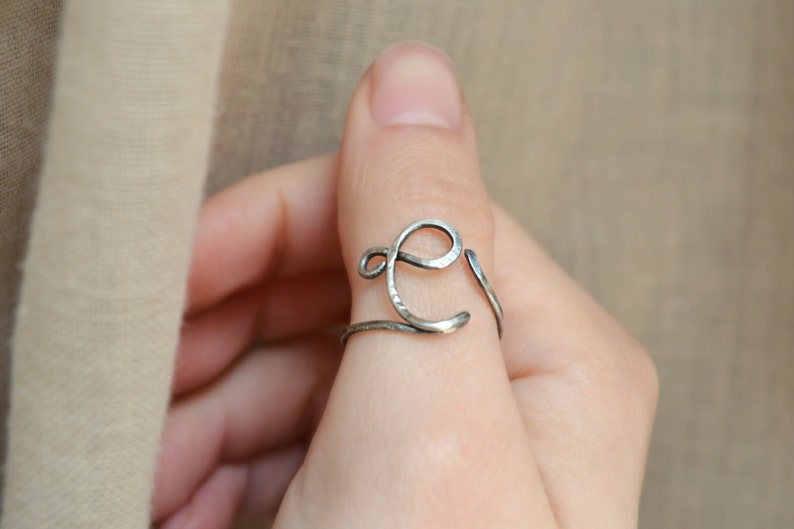 May include: A silver ring with a hammered finish, shaped like the letter E, worn on a finger.