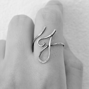 May include: A silver ring with a unique, abstract design. The ring is made of hammered metal and has a delicate, flowing shape.