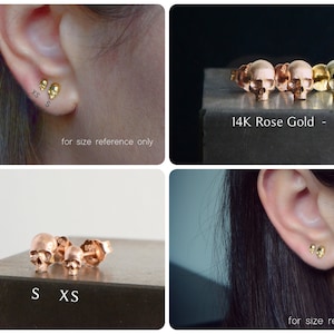May include: Two pairs of gold skull earrings in different sizes. The earrings are shown on a model's ear and on a surface. The text "S XS" and "14K Rose Gold - 14K Gold" is visible in the image.