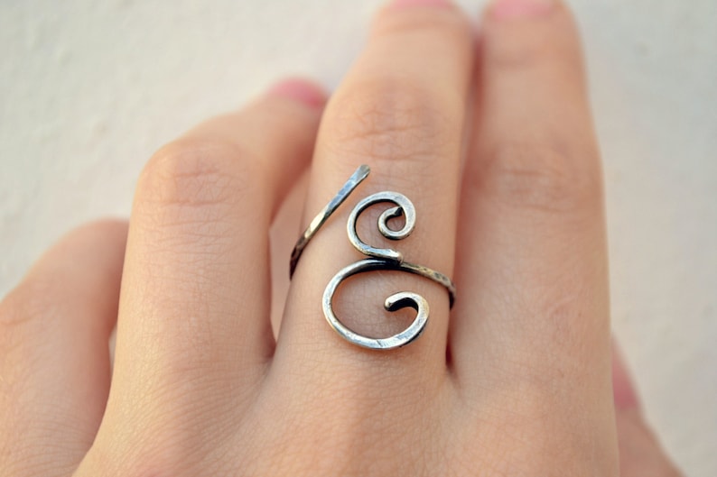 May include: A silver ring with a unique, swirling design. The ring is made of wire and has a hammered finish.