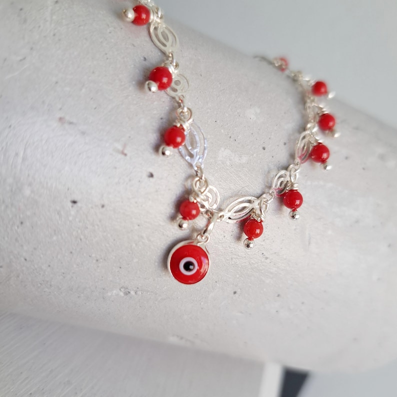 May include: Silver chain bracelet with red beads and a blue evil eye charm.
