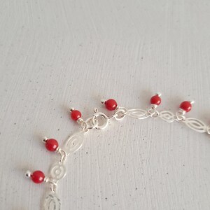 May include: A silver chain bracelet with red coral beads dangling from it. The bracelet has a lobster clasp closure.