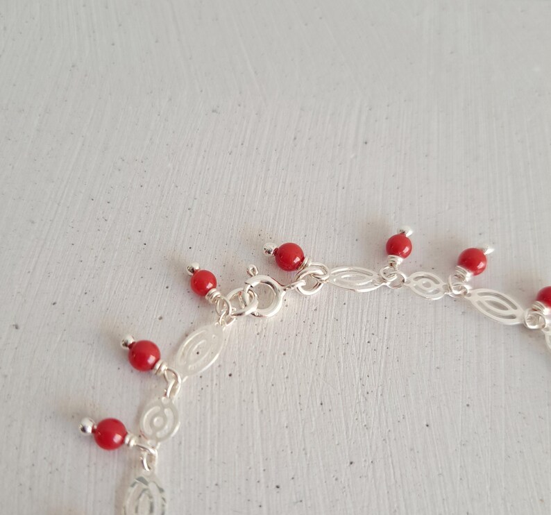 May include: A silver chain bracelet with red coral beads dangling from it. The bracelet has a lobster clasp closure.