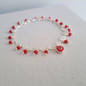 May include: A silver charm bracelet with a red evil eye charm and red bead accents.