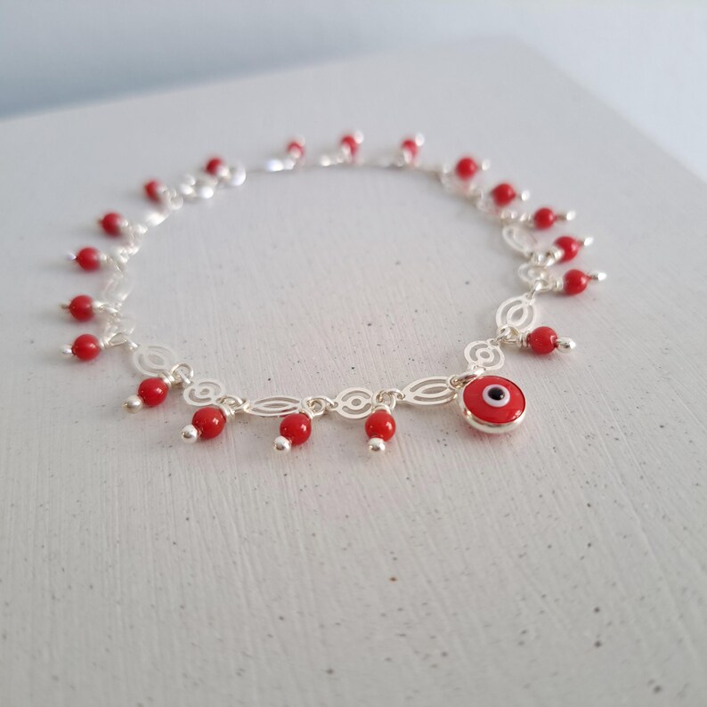 May include: A silver charm bracelet with a red evil eye charm and red bead accents.