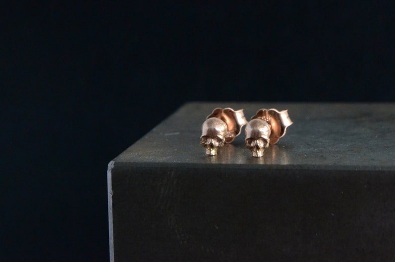 May include: A pair of gold skull stud earrings. The earrings are small and delicate, and they are perfect for adding a touch of edgy style to any outfit.
