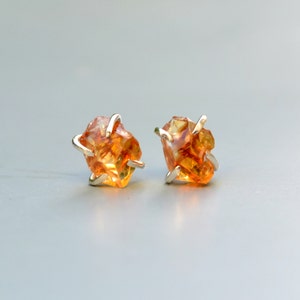 May include: A pair of silver earrings with orange gemstone accents. The gemstones are irregularly shaped and have a rough, natural look.