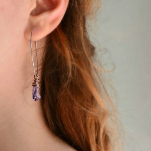 May include: A pair of silver earrings with a purple crystal pendant. The crystal is wrapped in copper wire.