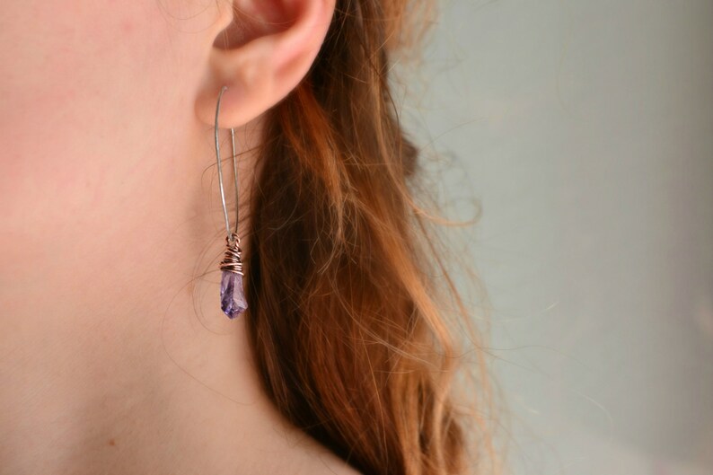 May include: A pair of silver earrings with a purple crystal pendant. The crystal is wrapped in copper wire.