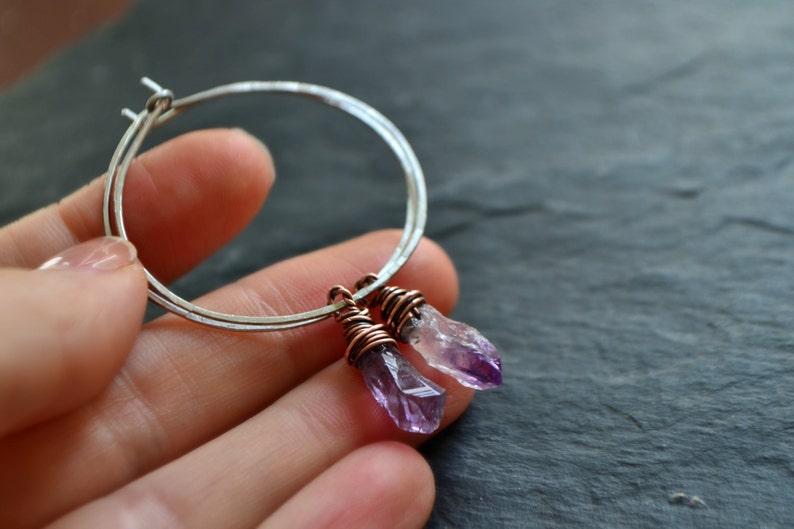 May include: Silver hoop earrings with two amethyst crystal drops wrapped in copper wire.