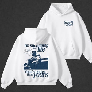 Pu&ograve; includere: Felpa con cappuccio bianca con tasca frontale e cappuccio. La parte anteriore della felpa con cappuccio presenta il testo "no such thing as a life that's better than yours" con una grafica blu di una persona. Il lato destro della felpa con cappuccio ha il testo "love yourz".