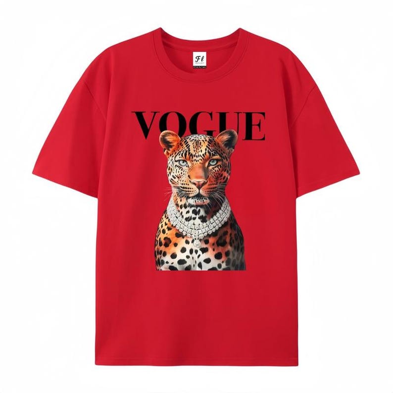 May include: Red t-shirt featuring a leopard wearing a diamond necklace. The word "VOGUE" is printed in black above the leopard's head. The shirt has short sleeves and a crew neck.