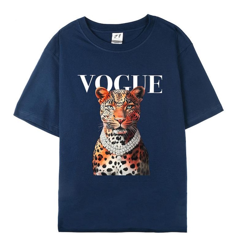 May include: Navy blue t-shirt featuring the word "VOGUE" in white above a leopard wearing a diamond necklace. The leopard has orange and black spots and is centered on the shirt.