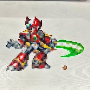 Könnte beinhalten: Pixelkunst eines roten, weißen und blauen Robotercharakters mit einem grünen Energiestrahl. Das Kunstwerk besteht aus kleinen, farbigen Perlen. Eine Münze liegt neben dem Kunstwerk zum Größenvergleich.