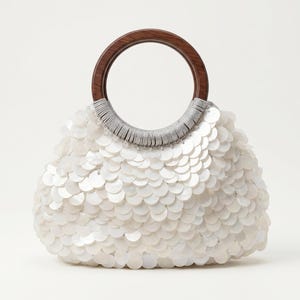 May include: A handbag covered in overlapping white circular sequins that create a scale-like texture. The bag features a round, dark brown wooden handle attached to the body with silver-colored thread wrapping at the base of the handle.