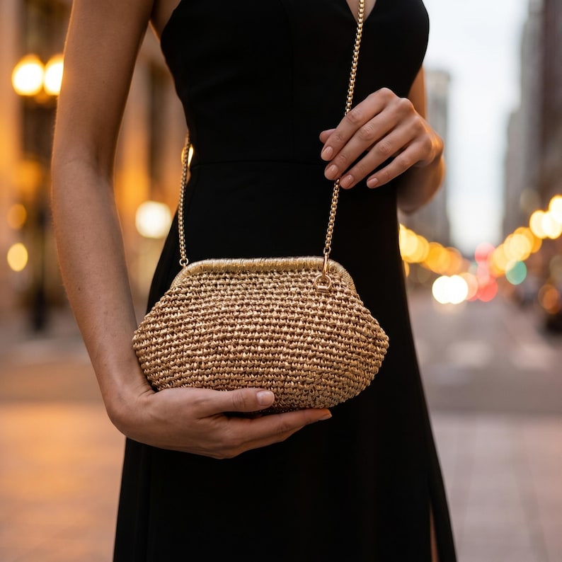 May include: A gold-toned woven clutch bag with a structured frame and a matching gold metal chain strap. The bag features a textured, crocheted-style surface with a metallic sheen and a secure clasp closure at the top, designed for carrying small items.