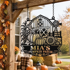 May include: A black metal hanging sign featuring a barn, windmill, corn stalks, pumpkins, and a sunflower. The sign includes a banner with the text "MIA'S PUMPKIN PATCH" and a small pumpkin icon at the bottom, suspended by two chains from a wooden beam.
