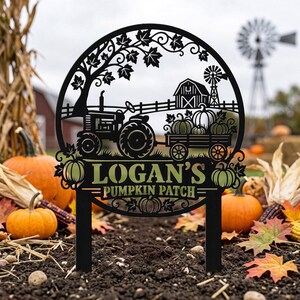 May include: A circular black metal garden sign featuring a cutout design of a tractor pulling a wagon filled with pumpkins. The sign includes a barn, a windmill, and maple leaves, with the text "LOGAN'S PUMPKIN PATCH" engraved in the centre.
