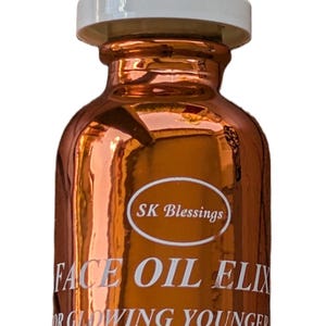 Puede incluir: Un frasco cuentagotas de vidrio de color cobre metálico con tapa blanca. La etiqueta presenta el texto SK Blessings, FACE OIL ELIXIR, FOR GLOWING YOUNGER SKIN, RELIEVES REDNESS, DRYNESS, ITCHING AND WRINKLES, y NET 1.0 FL. OZ. (29.6 ML).