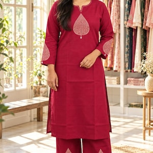 May include: A deep red long-sleeved kurta and wide-leg trousers set featuring white embroidered leaf motifs on the chest, sleeves, and pant hems. The tunic has a round neckline with a small slit and the fabric has a visible woven texture.