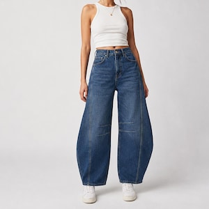 Puede incluir: Una camiseta de tirantes blanca acanalada combinada con vaqueros de mezclilla azul oscuro de talle alto, con una silueta ancha en forma de barril con costuras verticales prominentes en la parte delantera de cada pierna y zapatillas blancas.